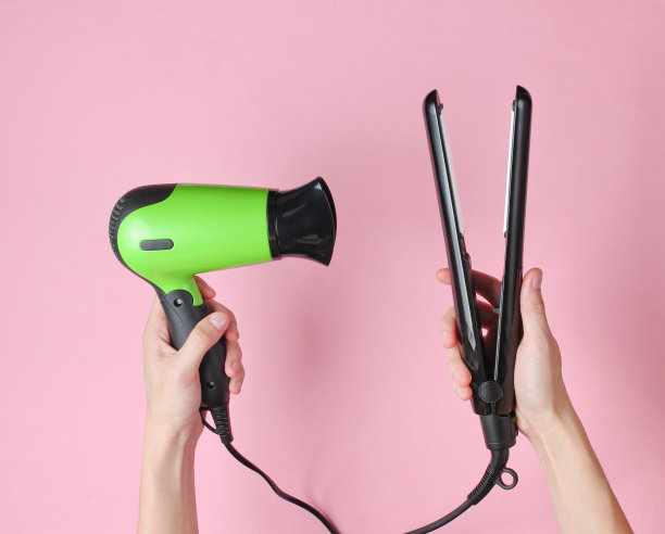 头发护理。粉色背景上的女性手拿着直发器和吹风机。俯视图图片下载