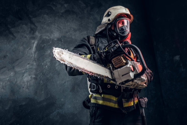 一个消防队员的肖像在安全头盔和氧气面罩拿着一个链锯。工作室照片对着深色纹理的墙图片下载