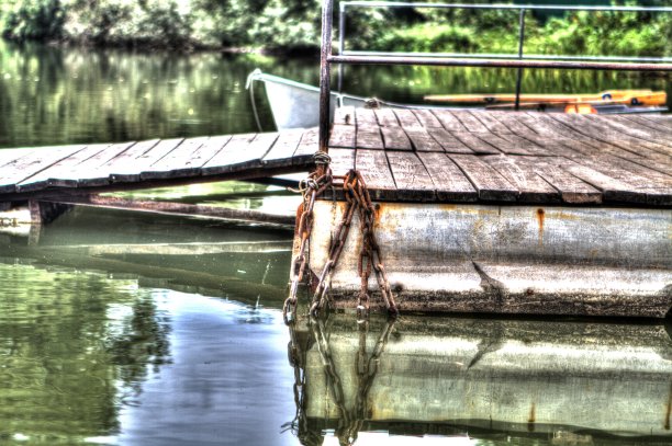 一根生锈的旧铁链在一个木码头边上放进水里。夏天，湖面上阴天图片下载