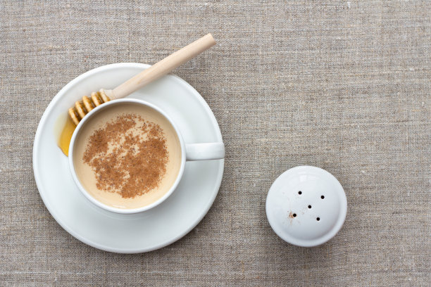 香喷喷的奶茶在一个白色瓷杯与蜂蜜和蜂蜜勺在纺织品的背景图片下载