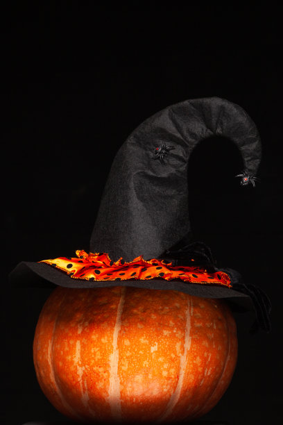 万圣节的庆祝活动。一个漂亮的橙色大南瓜上戴着一顶黑色女巫帽，上面有蜘蛛。设计。万圣节的象征概念。孤立的黑色背景图片下载
