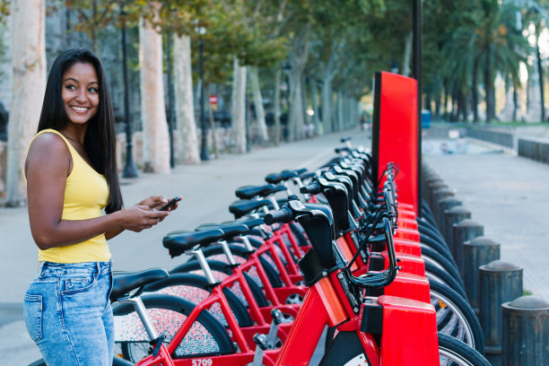 这是一个美丽的年轻女子在城市里租自行车时查看手机的照片图片下载