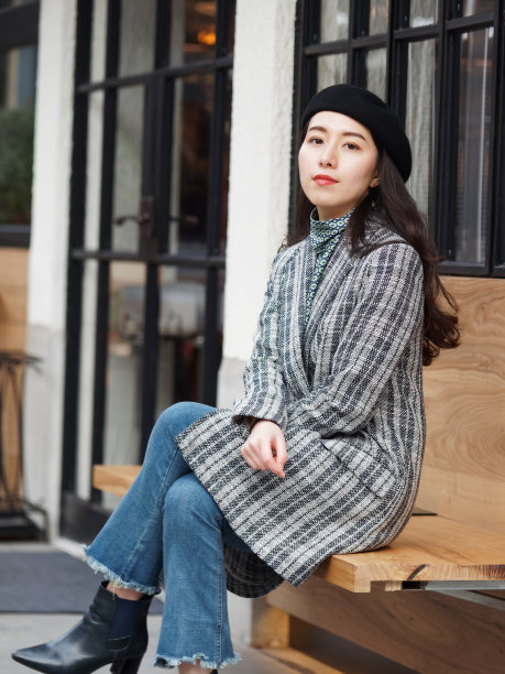 美丽的中国年轻女子穿着外套和牛仔裤坐在户外咖啡馆，看着镜头与腿交叉，自信的商业女性，户外时尚肖像魅力时尚女士。素材图片