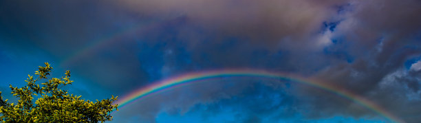 雨中的彩虹在蓝天和云的背景，阳光明媚的天气。图片下载