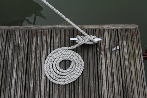 系泊用的棕色小船的绳子，卷在系柱上，末端整齐地叠在旁边。夏日湖面上的木码头。图片下载