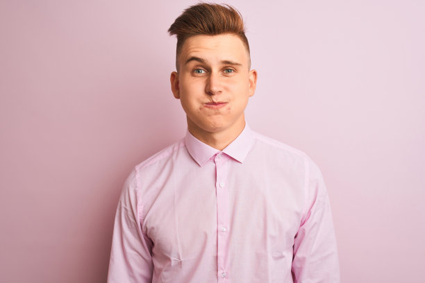 年轻英俊的商人穿着优雅的衬衫站在孤立的粉红色背景，鼓起的脸颊与滑稽的脸。嘴巴里充满了气，疯狂的表情。图片下载