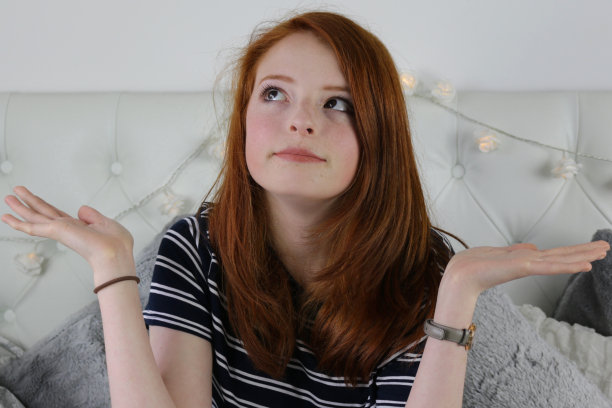 照片中，14 / 15岁的红头发少女，皮肤苍白，脸上有雀斑，脸颊通红，她穿着黑白条纹t恤，坐在卧室里，面带微笑，神情轻松图片下载