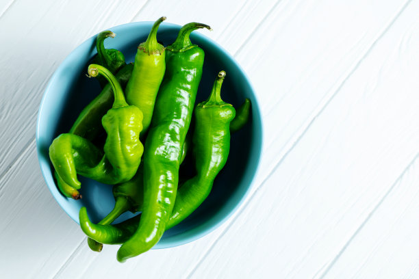 一个蓝色的碗里放着辛辣的青椒，背景是白色的木头，还有拷贝空间。顶视图的食物。不含硝酸盐、转基因的生态蔬菜。天然新鲜农产品。食物的照片背景图片下载