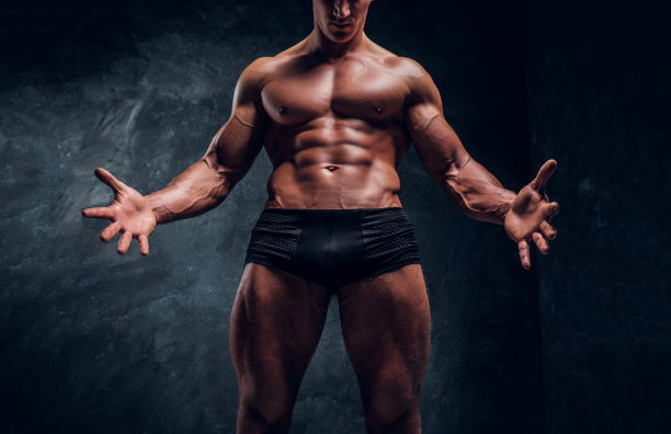 穿着内衣的运动员，展示着他完美的身体。工作室照片与黑暗的墙壁背景图片下载