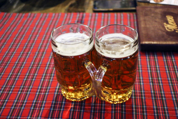 两杯新鲜的啤酒放在格子桌布上，象征着慕尼黑啤酒节。图片下载