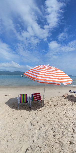 一把雨伞和沙滩椅在沙滩上，靠近大海，是放松的完美场景。图片下载