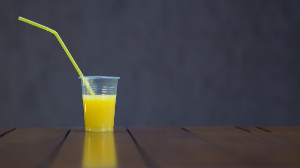 橙汁在一个塑料杯和一个管在一个棕色的背景。副本的空间。野餐，素食，健康食品，饮料。食品级塑料的再利用和回收图片下载
