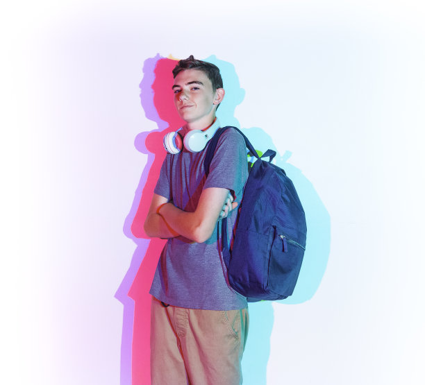 腰部以上/一个男人只有12-13岁英俊的人白人男性男孩/十几岁的男孩/学生/高中生/初中生前面的白色背景，穿着背包/ t恤/衬衫双臂交叉和拿着包图片下载