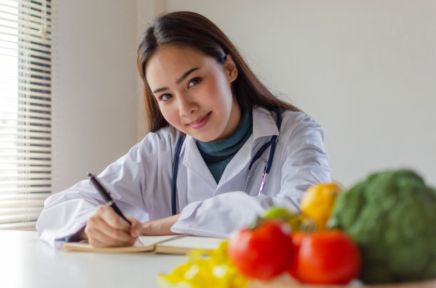 年轻的营养学家女医生或医生看着相机写饮食计划和新鲜的蔬菜，水果在实验室办公室的桌子上，营养，健康的生活方式，健康的食物，节食的概念图片下载
