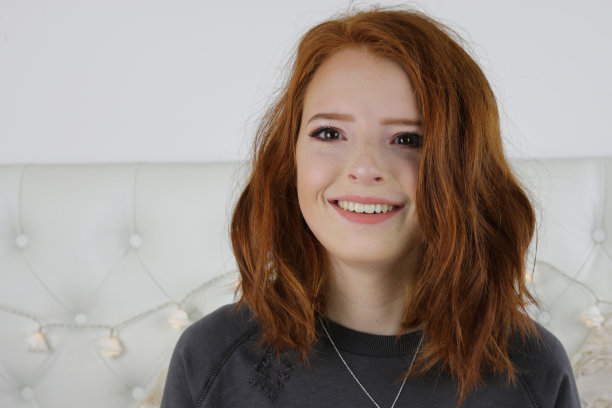 这张照片是一个14 / 15岁的红头发、皮肤苍白、长着雀斑的少女，她坐在卧室里试着在嘴唇上涂裸色的口红，嘴唇在仙女线灯光的照射下撅起，这是一张特写的自然脸的妆容图片下载