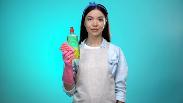 漂亮的家庭主妇在围裙上拿着海绵和洗洁精，清洗图片下载