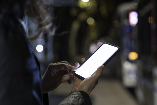 晚上在公交车站等车时，拿着空白手机的女人。图片下载