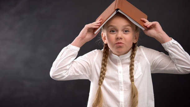 滑稽的女孩头上顶着书在黑板上晃悠，学校生活图片下载