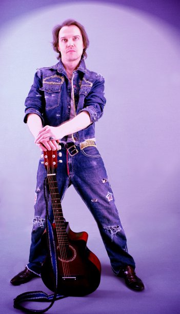 酷酷的摇滚吉他手穿着牛仔裤西装站在旁边的原声吉他在一个彩色的背景。在一个场景中表演的音乐家图片下载