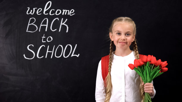 可爱的微笑女孩拿着一束郁金香在黑板旁欢迎回到学校图片下载