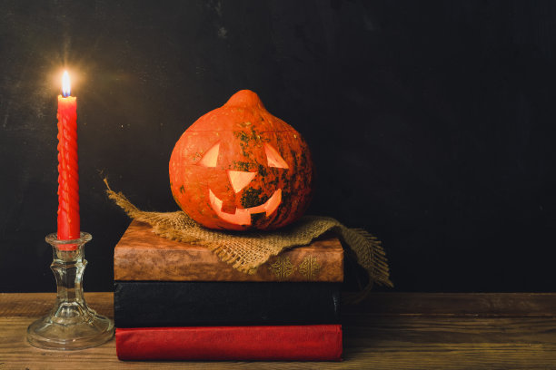 万圣节南瓜堆在一堆书旁边，旁边有一支燃烧的蜡烛图片下载