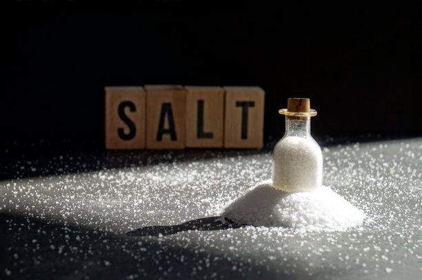 旧的微型玻璃放在一堆盐上，黑色背景上的木方上的单词。图片下载