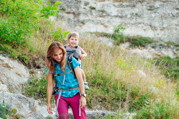 微笑的小女孩在背包承运人徒步旅行与她的母亲图片下载