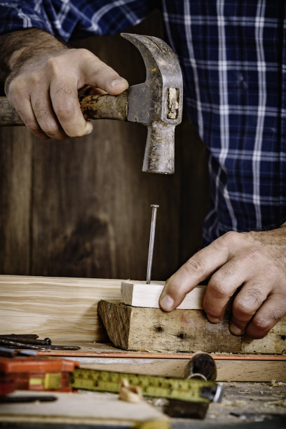 成熟的木匠使用锤子和钉子在家庭车间木板的特写图片下载