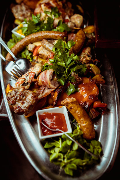 近距离的照片混合烤肉拼盘。牛肉，猪肉，家禽，香肠，烤大蒜，辣椒，红色的西红柿在木制的乡村背景。图片下载