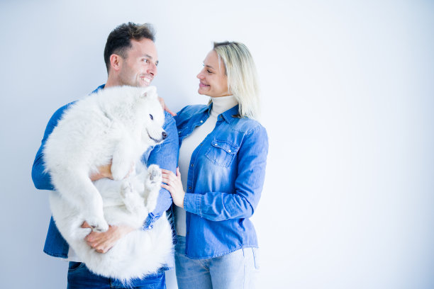 年轻美丽的夫妇抱着狗站在孤立的白色背景图片下载