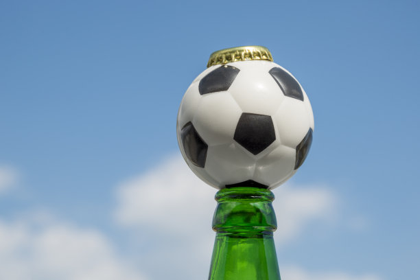 一瓶开着的啤酒和一个对着天空的足球。图片下载