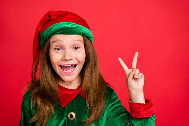 近距离的照片，欢快的节日精灵孩子长红色的头剪在绿色的帽子穿着精灵服装使v字孤立在红色的背景图片下载