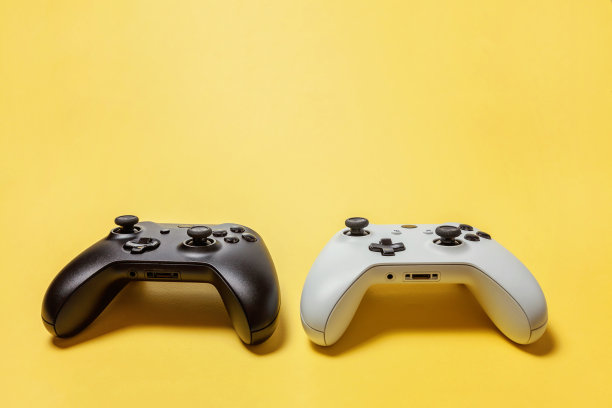 白色和黑色两个操纵杆在黄色背景上。电脑游戏竞赛电子游戏控制对抗概念图片下载