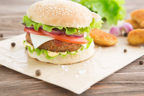 美味的快餐。芝士汉堡配上烤肉、芝士、番茄，放在牛皮纸上，贴在木板上。快餐模板。真实的照片。理想的广告图片下载