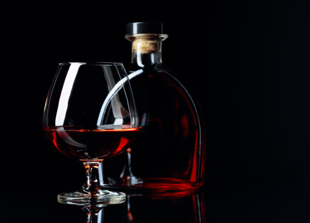 玻璃和一瓶白兰地在一个黑色反光的背景。图片下载