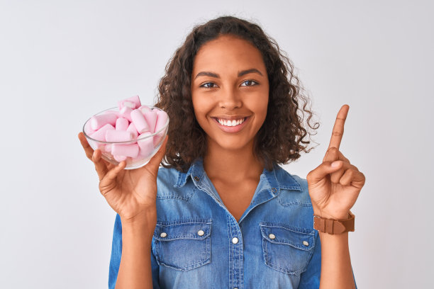 年轻的巴西妇女拿着一个有棉花糖的碗，在孤立的白色背景下惊讶地提出一个想法或问题，用快乐的脸指着手指，第一图片下载