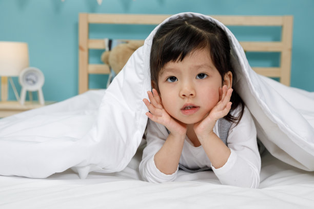 小女孩在她卧室的木床上盖着毯子，快乐的亚洲小女孩睡在床上图片下载