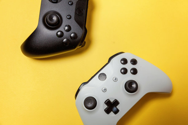 白色和黑色两个操纵杆在黄色背景上。电脑游戏竞赛电子游戏控制对抗概念图片下载