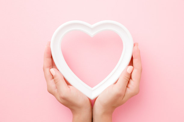 年轻女子手握白色的心框在淡粉色的背景。爱和幸福的概念。为可爱的，情绪化的，感伤的文字，引用或语录空的地方。特写镜头。前视图。图片下载