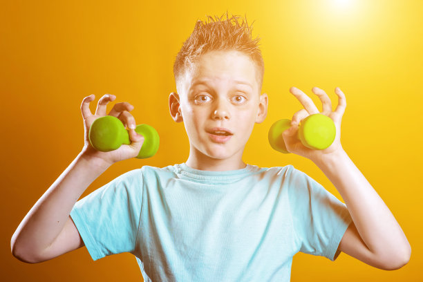 一个穿着亮t恤黄色背景上有哑铃的男孩图片下载