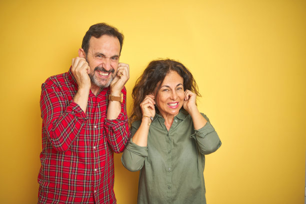 美丽的中年夫妇在孤立的黄色背景覆盖耳朵与手指与烦恼的表情大声的音乐噪音。聋的概念。图片下载