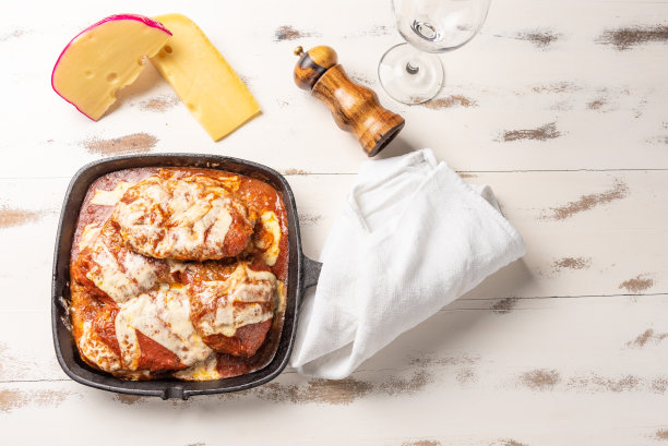 帕尔玛芝士牛排也称为帕尔玛芝士腓力牛排在一个黑色的铁锅，在木制的白色背景，奶酪和番茄酱。图片下载