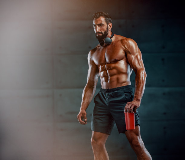 英俊的肌肉男拿着蛋白质饮料，脖子上挂着无线耳机图片下载