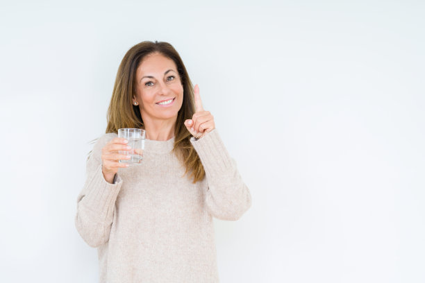 中年妇女喝着一杯水孤立的背景，惊讶地用一个想法或问题指着幸福的脸，第一图片下载