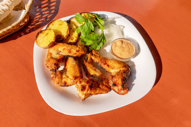 炸鸡翅放在盘子里，配菜是炸土豆和新鲜的香草放在红色的桌子上。近距离图片下载