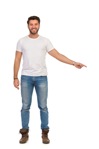 微笑英俊的男人在牛仔裤和白色t恤站着，指向下，看着相机。前视图。图片下载