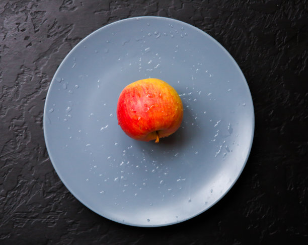 一个苹果躺在灰色的盘子里。静物照片。黑色背景。图片下载
