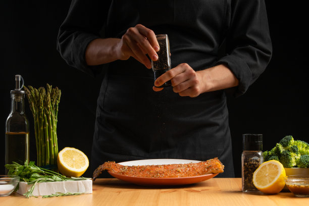 厨师烹饪海鲜，红色鱼撒胡椒，鲑鱼或鳟鱼在黑色的背景。运动，餐厅菜单，食谱书，亚洲菜，自制食谱。广场的照片图片下载