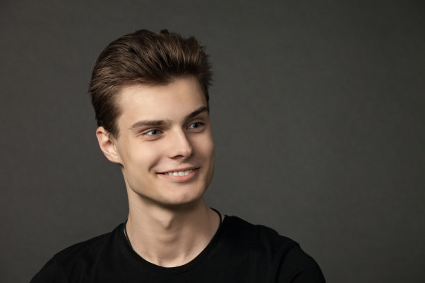 一个迷人的18岁男子在一个黑色背景的黑色t恤的工作室肖像图片下载