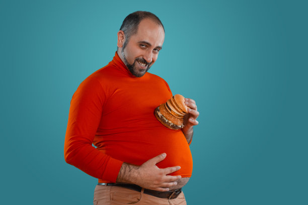 一个留着胡子的中年男子的特写，穿着红色高领毛衣，摆姿势与汉堡在蓝色背景下。快餐图片下载